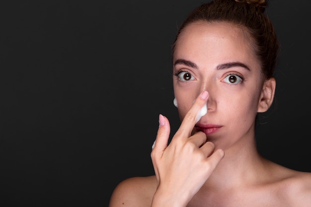 Mujer joven que aplica la crema de nariz