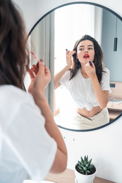 Mujer joven que aplica el lápiz labial que mira el espejo