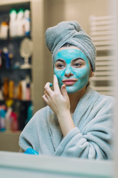 Mujer joven que aplica la máscara azul