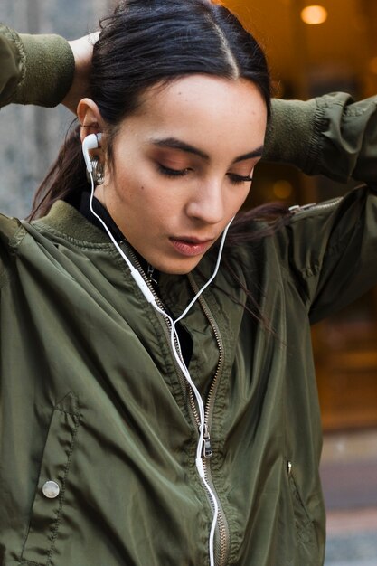 Mujer joven que ata su música que escucha del pelo en el auricular