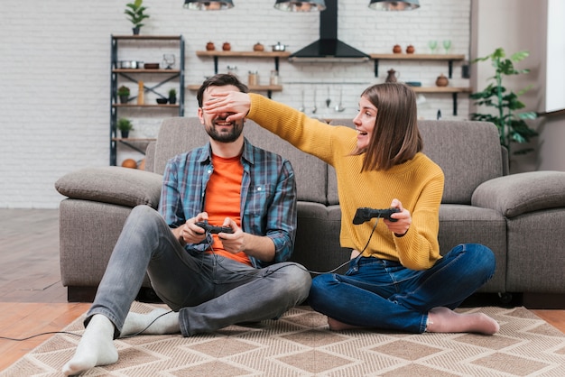 Mujer joven que se burla de su marido jugando el videojuego en casa