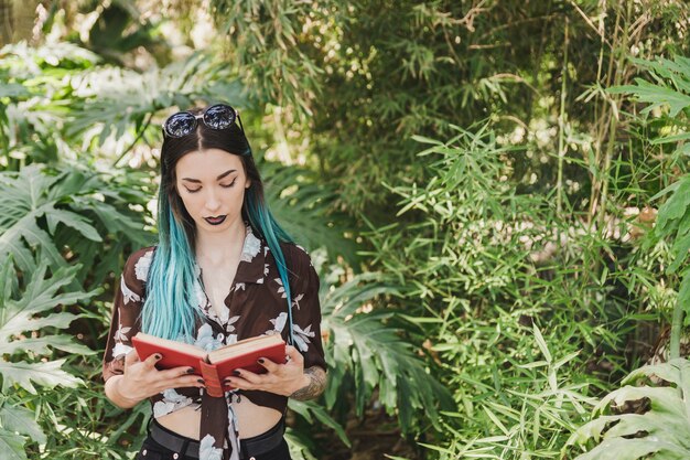 Mujer joven que se coloca delante del libro de lectura creciente de las plantas