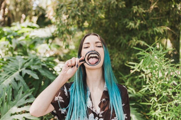 Mujer joven que se coloca delante de las plantas que muestran la lengua a través de la lupa