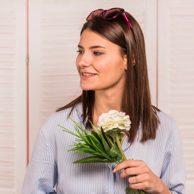 Mujer joven que se coloca con la flor blanca a disposición