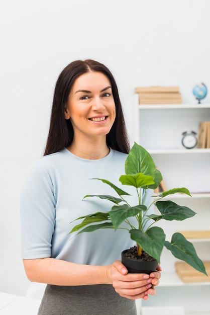 Mujer joven que se coloca con la planta verde en maceta