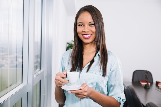 Foto gratuita mujer joven que se coloca con la taza de café en oficina