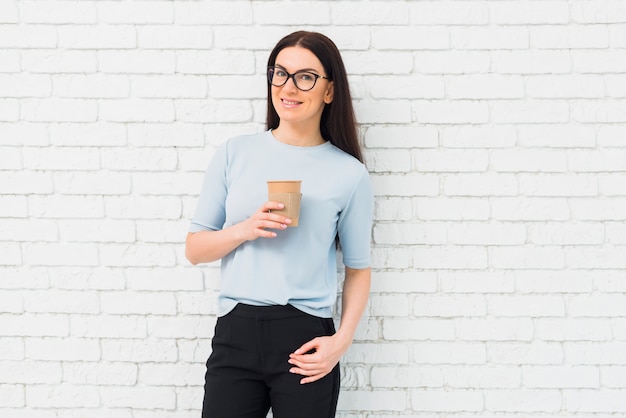 Mujer joven que se coloca con la taza de café