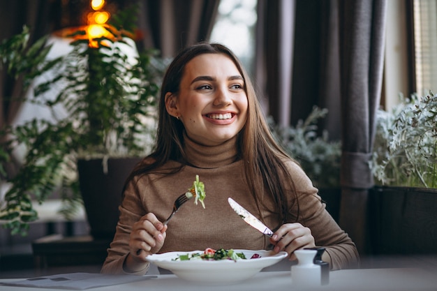 Mujer joven que come la ensalada en un café