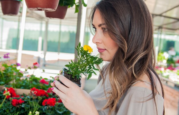 Mujer joven que compra flores en un centro de jardinería. Mis flores favoritas. Mujer que mira las flores en una tienda. Retrato de una mujer sonriente con flores en vivero de plantas