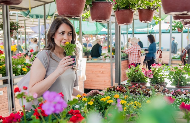 Mujer joven que compra flores en un centro de jardinería. Mis flores favoritas. Mujer que mira las flores en una tienda. Retrato de una mujer sonriente con flores en vivero de plantas