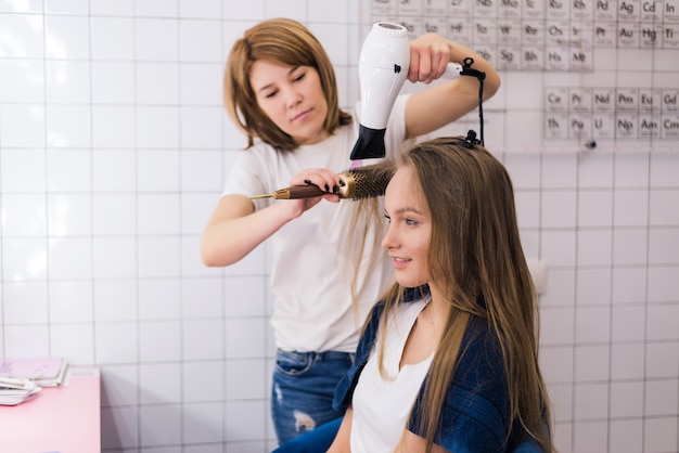 Mujer joven que consigue un nuevo peinado con secador en el salón de peluquería profesional.