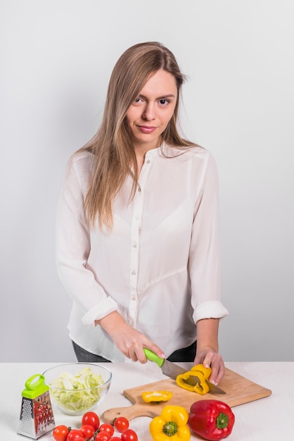 Foto gratuita mujer joven que corta la pimienta amarilla en el tablero de madera