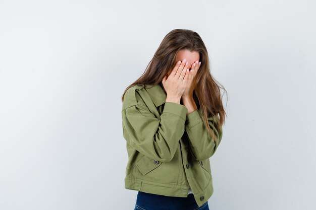 Mujer joven que cubre la cara con las manos en camisa, chaqueta y mirando emocionado, vista frontal.