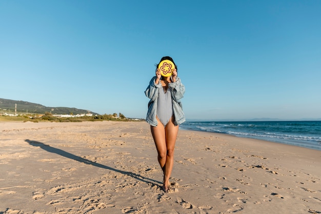 Mujer joven que cubre la cara con la placa del disco volador en la playa
