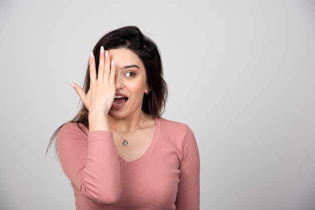 Foto gratuita mujer joven que cubre un ojo con la mano y mirando a la cámara.