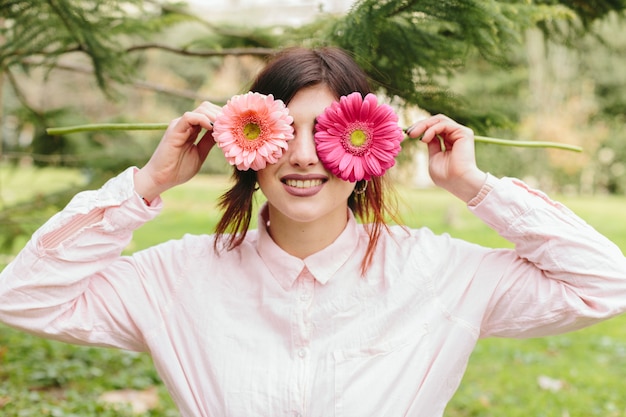 Mujer joven que cubre ojos flores y sonriendo