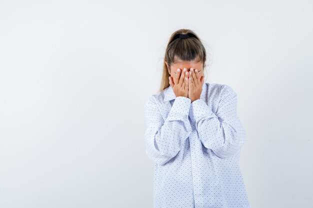 Mujer joven que cubre el rostro con las manos en la camisa blanca y mirando acosado