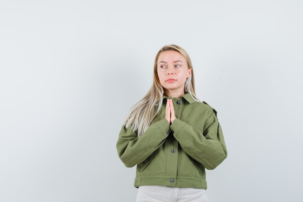 Mujer joven que desea en chaqueta verde, jeans, vista frontal.