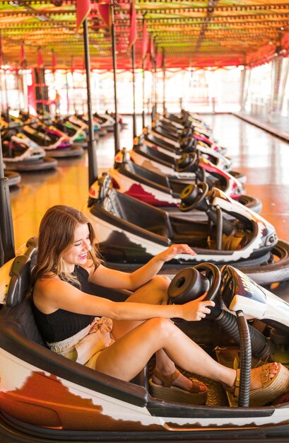 Mujer joven que disfruta conduciendo el coche de parachoques en el parque de atracciones