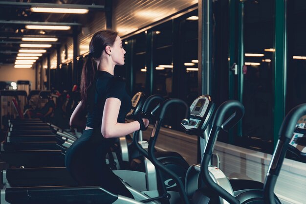 Mujer joven que ejercita en la máquina cardio elíptica