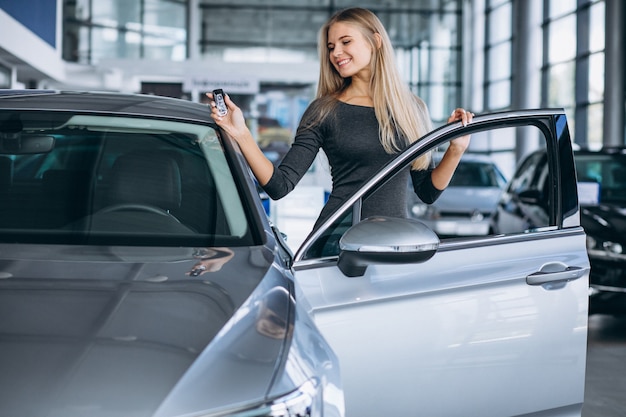 Mujer joven que elige un coche en un showroom de automóviles