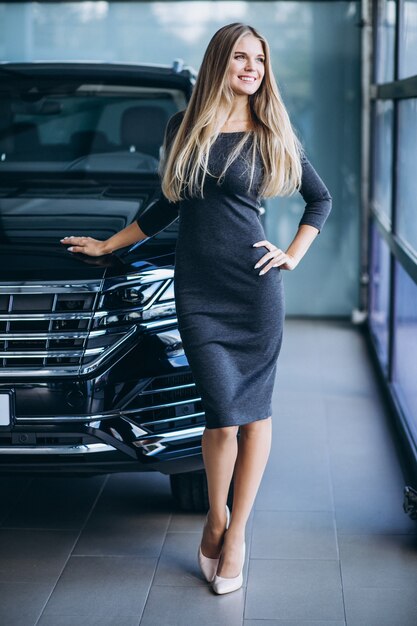 Mujer joven que elige un coche en un showroom de automóviles