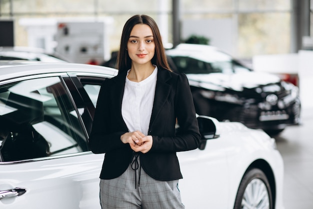 Mujer joven que elige un coche en un showroom de automóviles