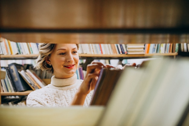 Mujer joven que elige el libro en la biblioteca