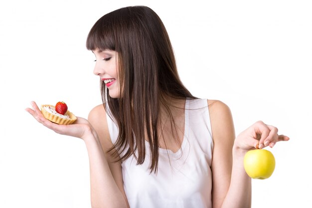 Mujer joven que elige la torta en vez de la manzana