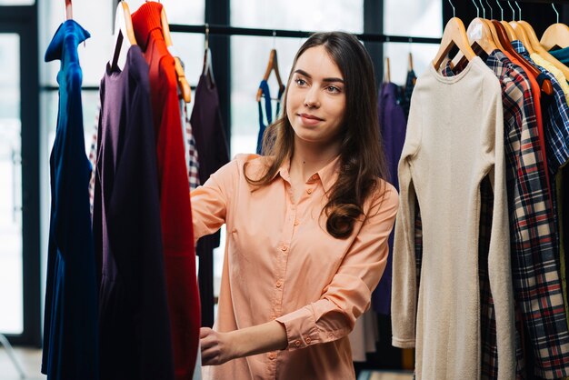 Mujer joven que elige vestidos en la tienda