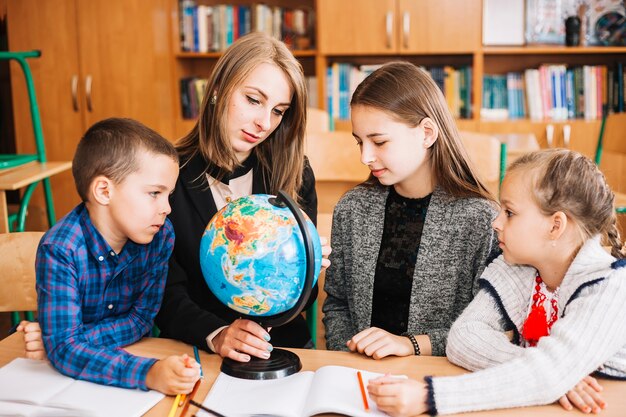 Mujer joven que enseña la geografía al alumno con globo