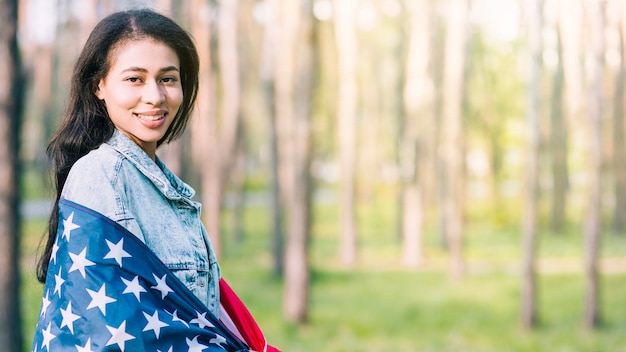 Mujer joven que envuelve en bandera americana en naturaleza