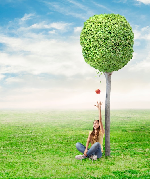 mujer joven que es sorprendido por una manzana roja debajo de un árbol