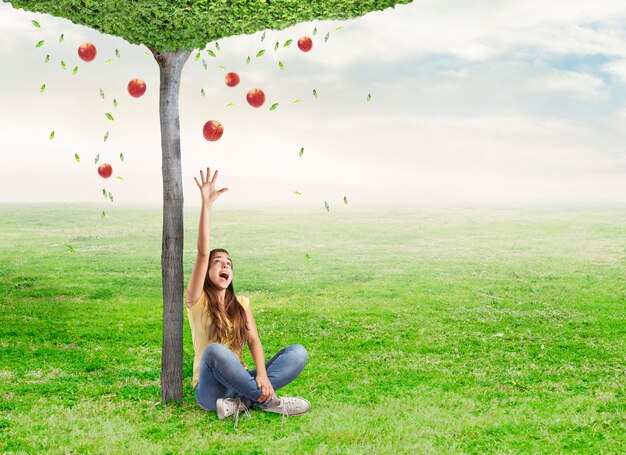 mujer joven que es sorprendido por una manzana roja debajo de un árbol