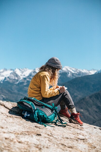 Una mujer joven que escribe en su libro de texto mientras está sentada en una colina cerca de una montaña