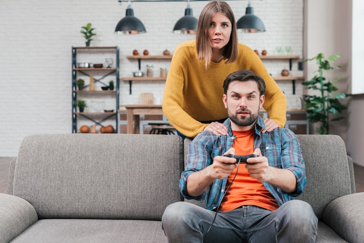 Foto gratuito mujer joven que está parada detrás de su marido que se sienta en el sofá que juega al videojuego