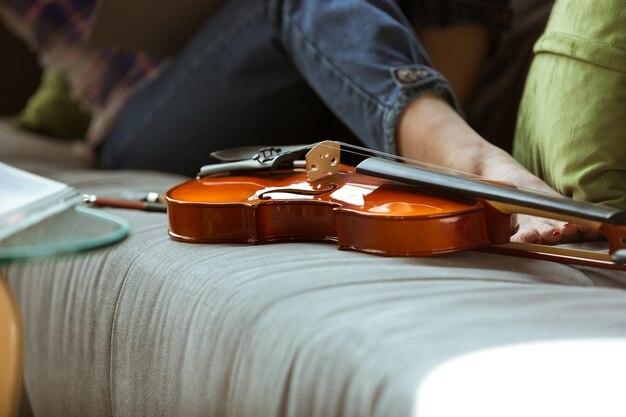 Foto gratuita mujer joven que estudia en casa durante cursos en línea o información gratuita por sí misma. se convierte en músico, violinista mientras está aislado, cuarentena contra la propagación del coronavirus. usando computadora portátil, teléfono inteligente.