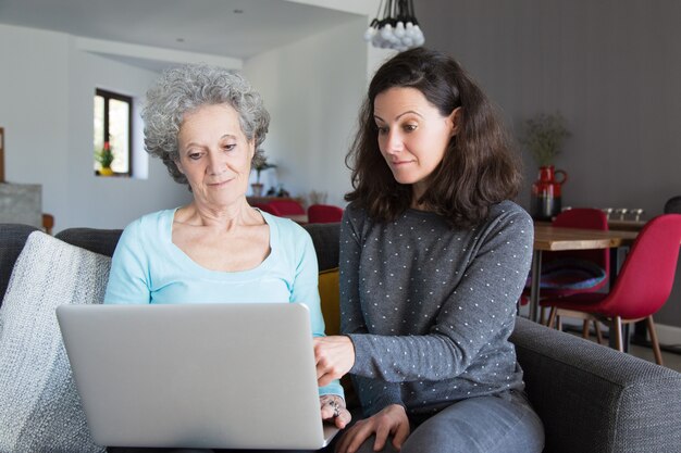 Mujer joven que explica a la abuela cómo utilizar la computadora portátil