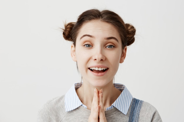 Foto gratuita mujer joven que expresa la positividad y la felicidad de pie con las palmas juntas sobre la pared blanca. chica sincera morena pidiendo a sus padres que vayan al campamento de verano gesticulando con las manos. de cerca