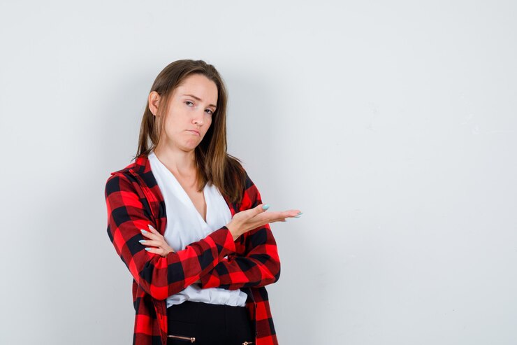 Foto gratuito mujer joven que finge mostrar algo en ropa casual y parece reacio, vista frontal.