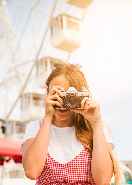 Mujer joven que fotografía con la cámara en el parque de atracciones