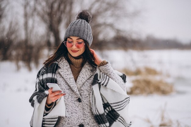 Mujer joven que habla en el teléfono afuera en el parque de invierno