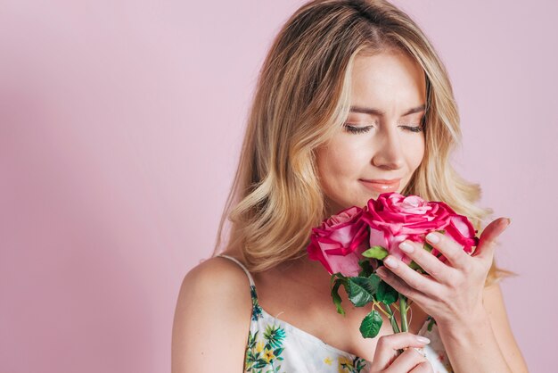 Mujer joven que huele las rosas contra fondo rosado