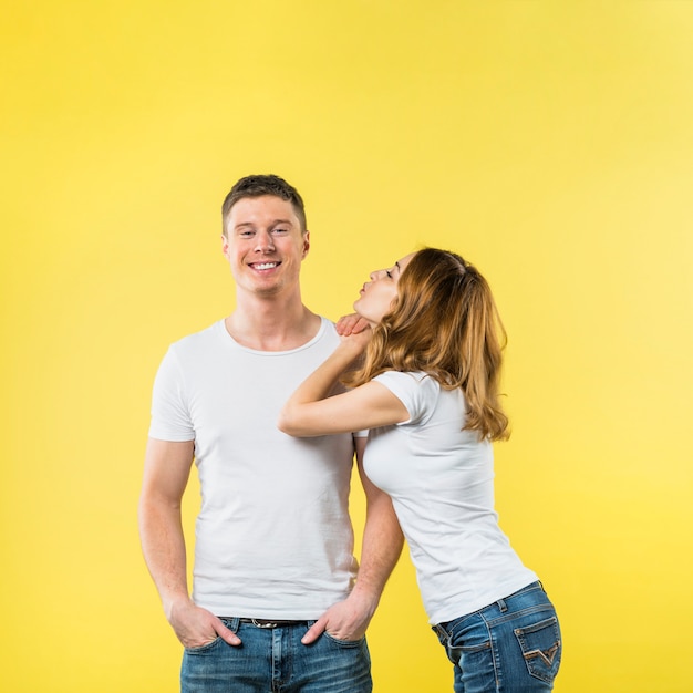 Mujer joven que se inclina en el beso que sopla del hombro de su novio contra el contexto amarillo