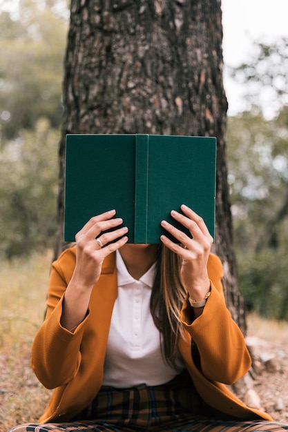 Mujer joven que lee el libro que se sienta debajo del árbol