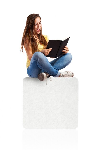 mujer joven que lee un libro sentada en una caja blanca
