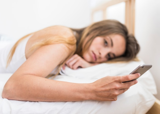 Mujer joven que miente en cama usando el teléfono móvil