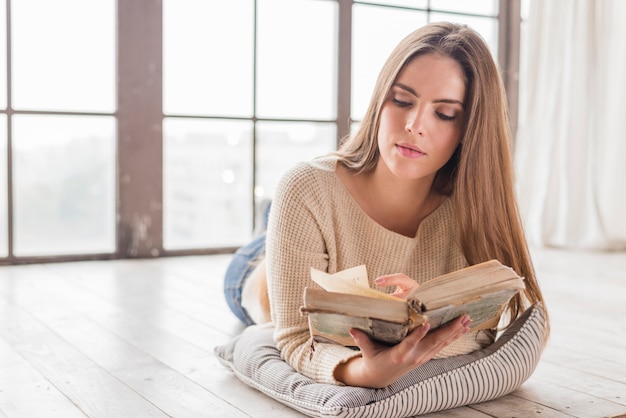 Mujer joven que miente cerca del libro de lectura de la ventana