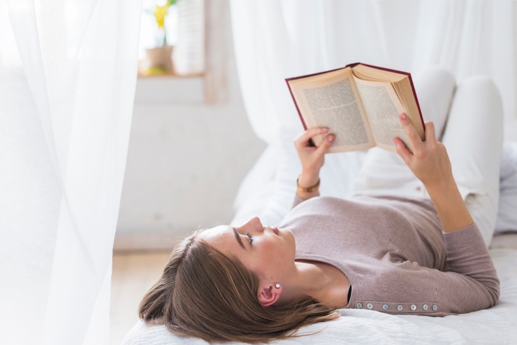 Foto gratuito mujer joven que miente en el libro de lectura de la cama