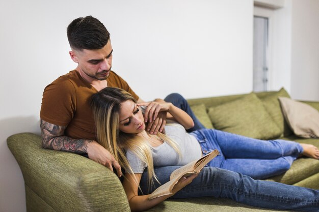 Mujer joven que miente en el regazo de novio en el libro de lectura del sofá